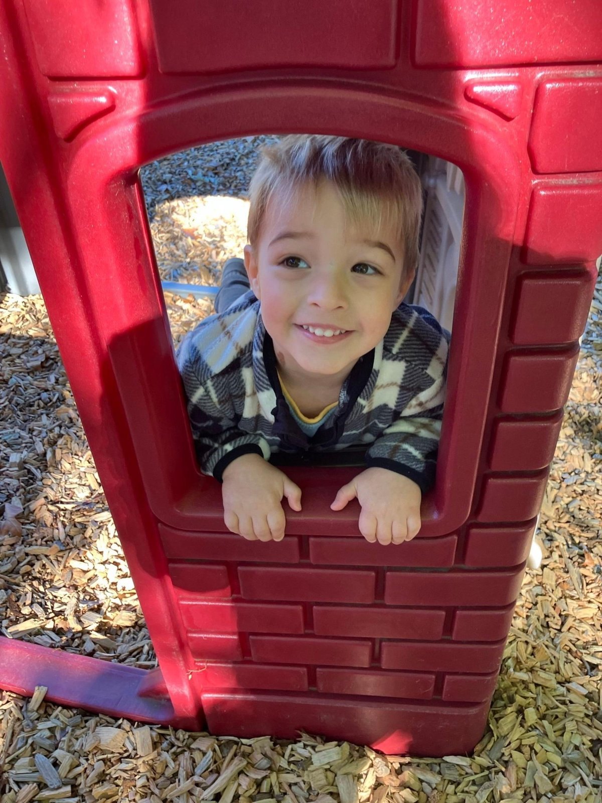 Smiling child peeking out of the playhouse on the ACNS playground in Newton
